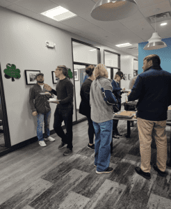 People are standing and talking in a room with food on a table. Walls are decorated with framed pictures and clovers.