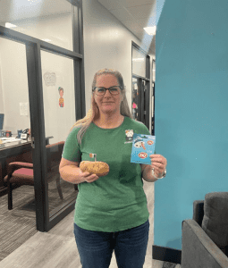 Person in green shirt holding a large potato and Dairy Queen gift cards, standing in an office hallway.