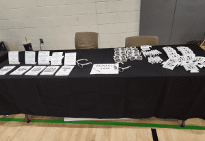 A table with a black tablecloth displays informational pamphlets, McNeel Law-branded sunglasses, buttons, and pens at an indoor event.
